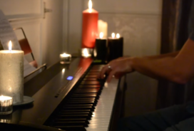 Man playing piano from a side view with visible hands and arms, surrounded by candles on and around the piano